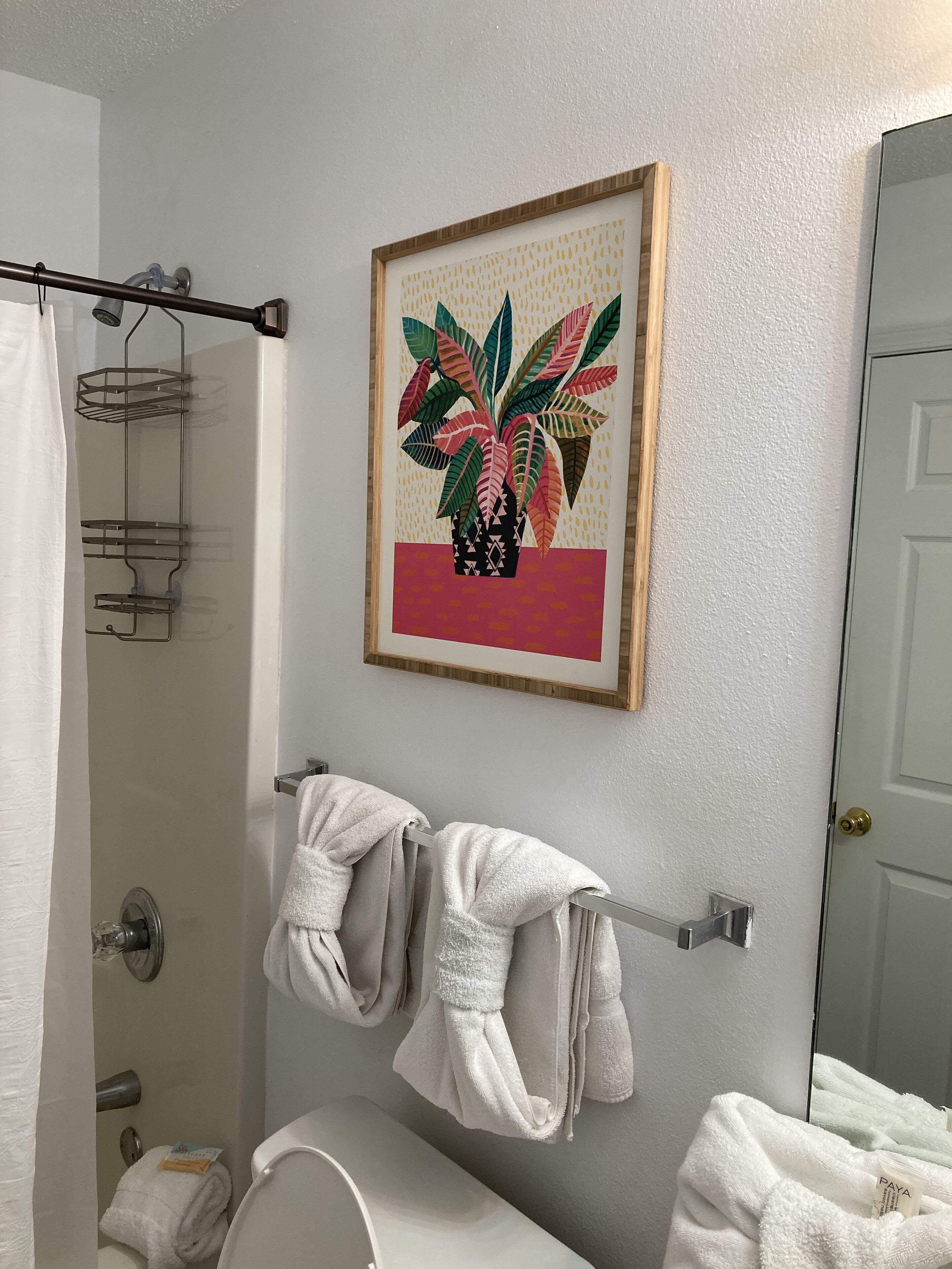 A bathroom with a shower, a towel rack with towels, and a framed artwork on the wall.