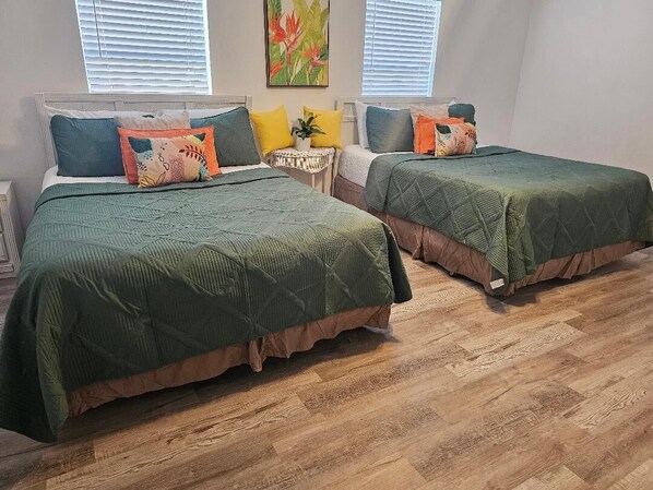 A bedroom with two beds, a small side table, and a window with blinds.