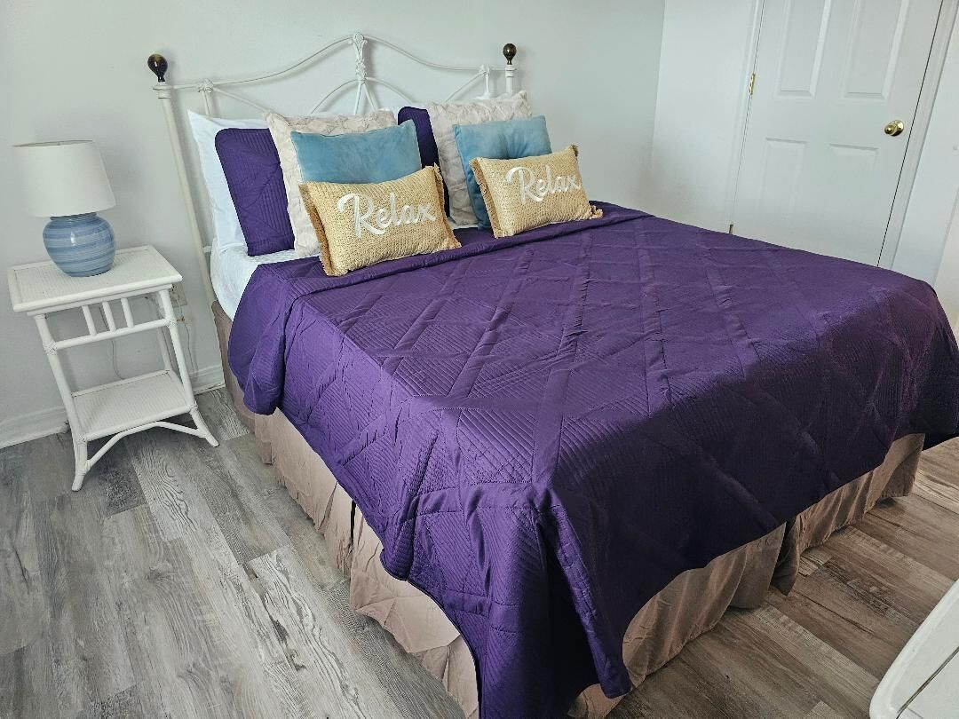 A bedroom with a bed, pillows, a nightstand, and a lamp.