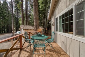 A wooden deck with a metal table and chairs, surrounded by tall trees. - Glades Getaway by Tahoe Getaways- North Shore 3 BR - Dog OK (Carnelian Bay)