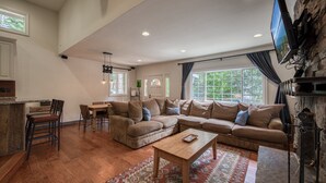 Uma sala de estar ampla com um sofá seccional grande, uma mesa de centro de madeira e uma lareira de pedra.