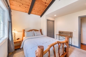 A bedroom with a bed, bedside table, lamp, and a bench.