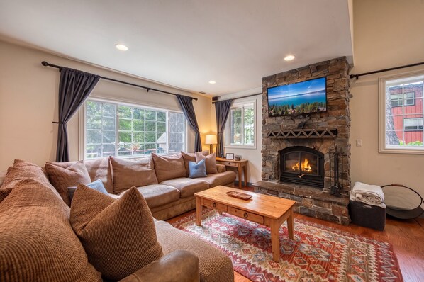 A living room with a stone fireplace, a large window, and a sofa with cushions.