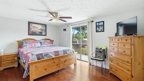 A bedroom with a wooden bed, a ceiling fan, a dresser, and a television.