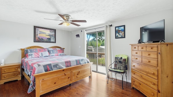 Une chambre avec un lit en bois, un ventilateur de plafond, une commode et un téléviseur.