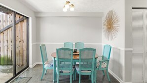 A dining area with a round table and six turquoise chairs, a ceiling light fixture, and a decorative wall piece.