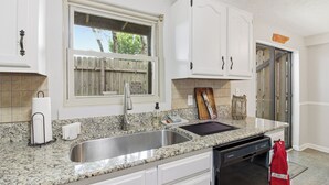 A kitchen with granite countertops, stainless steel sink, white cabinets, a wooden cutting board, and a red towel hanging on the door.