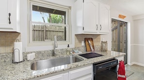 A kitchen with granite countertops, stainless steel sink, white cabinets, a wooden cutting board, and a red towel hanging on the door.