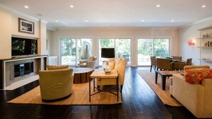Un salon spacieux doté d’une cheminée, de sièges confortables et de grandes fenêtres offrant une vue sur l’extérieur.
