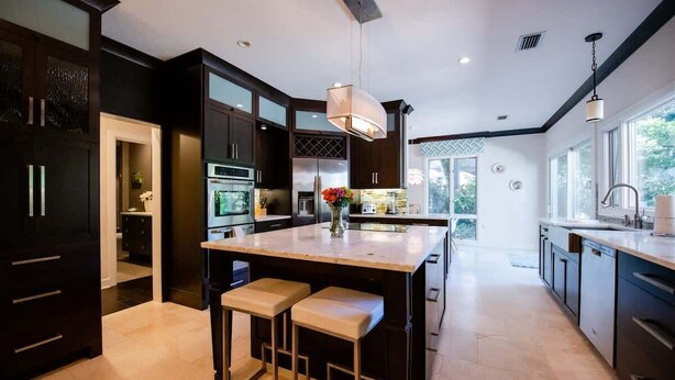 Une cuisine moderne avec des meubles de couleur sombre, un grand îlot central doté de tabourets et un luminaire suspendu.