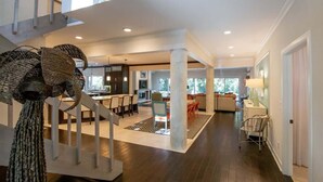 Un intérieur spacieux avec un espace central ouvert, un escalier et une cuisine à l’arrière-plan.