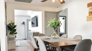 Un coin repas avec une table en bois, des chaises, un vase avec des plantes et un téléviseur à écran plat fixé au mur.