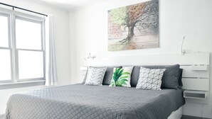 Une chambre moderne avec un grand lit, une fenêtre et une œuvre d’art accrochée au mur.