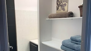 A bathroom with white tiles, a towel rack with blue towels, a shelf with a 'Seafood' sign, and a dark-colored cabinet.