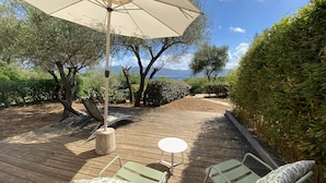 A wooden deck with lounge chairs and a table, surrounded by greenery and a view of the sea.