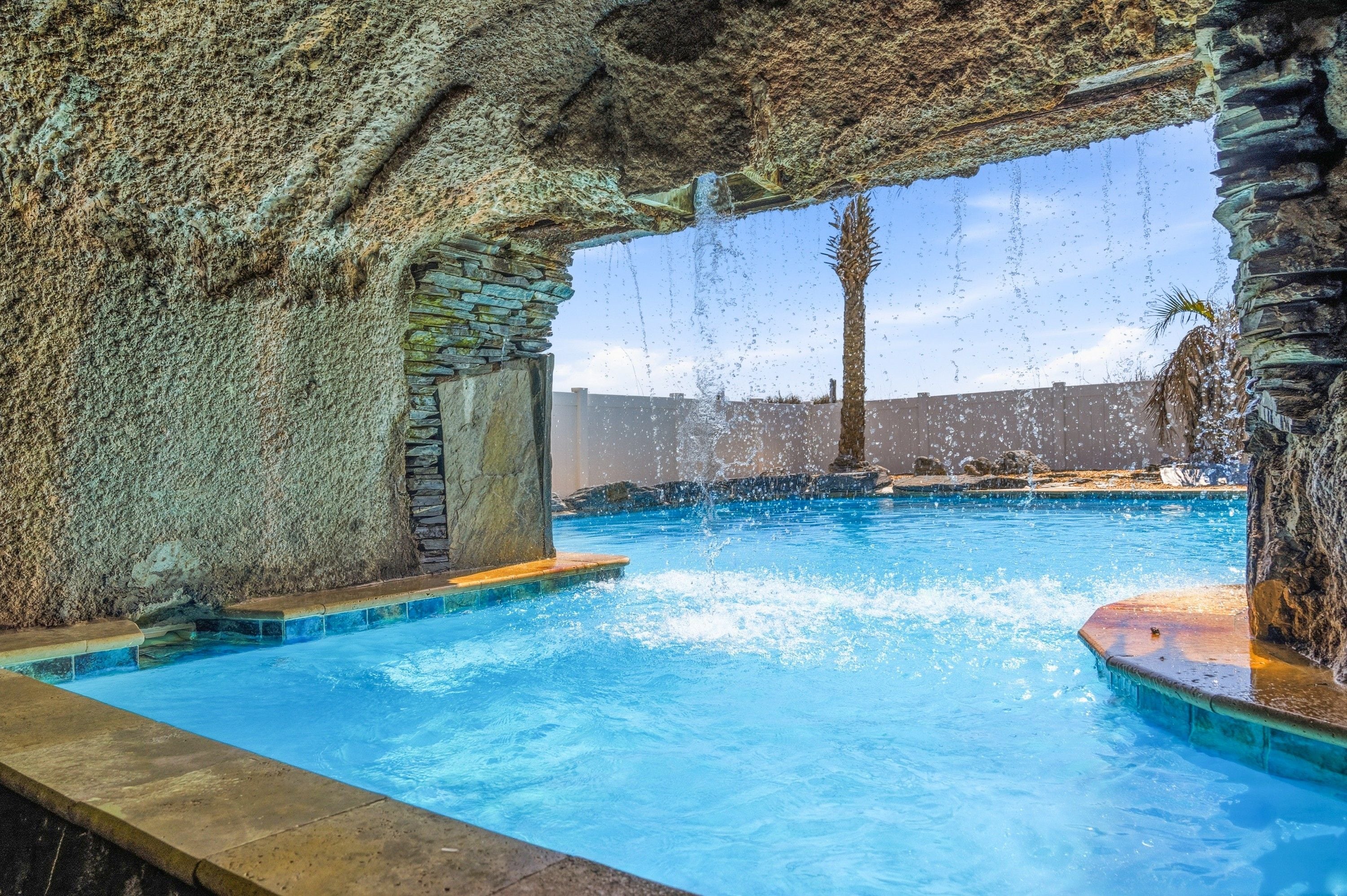 Una piscina con hidromasajes, paredes de piedra y una palmera.