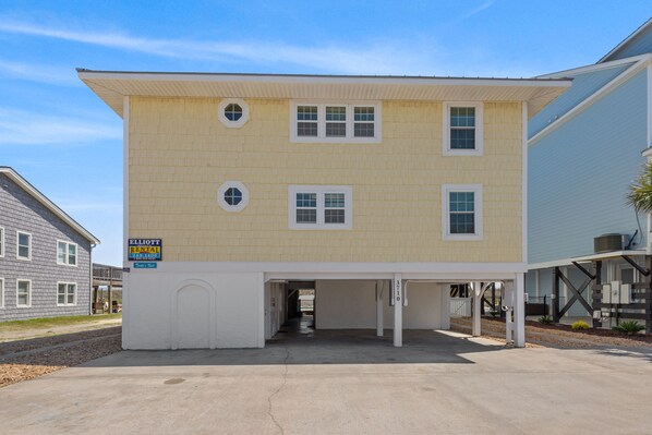A two-story building with a yellow exterior, a covered parking area, and a sign indicating rental availability. - 2 Night Minimum Stay in Off Season - Pet Friendly 8BR Oceanfront Home in Cherry Grove, Game Room & Beautiful Pool (ISLELAG) (North Myrtle Beach)