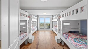 A room with bunk beds, a wooden floor, and a view through a glass door. - 2 Night Minimum Stay in Off Season - Pet Friendly 8BR Oceanfront Home in Cherry Grove, Game Room & Beautiful Pool (ISLELAG) (North Myrtle Beach)
