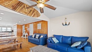A spacious living area with a wooden ceiling, a ceiling fan, a blue sofa set, and a wooden dining table. - 2 Night Minimum Stay in Off Season - Pet Friendly 8BR Oceanfront Home in Cherry Grove, Game Room & Beautiful Pool (ISLELAG) (North Myrtle Beach)