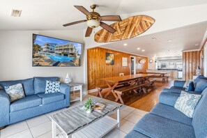 A spacious living room with a large sofa set, a wooden dining table, and a ceiling fan.