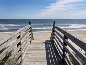A wooden boardwalk leading to a beach with waves in the background.
