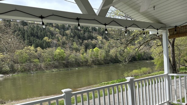A covered outdoor area with a white railing, a view of a river, and string lights.