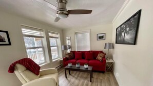 A living room with a red sofa, a white armchair, a coffee table, and a ceiling fan.