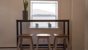 A small room with a window, two wooden stools, and two potted plants on the windowsill.