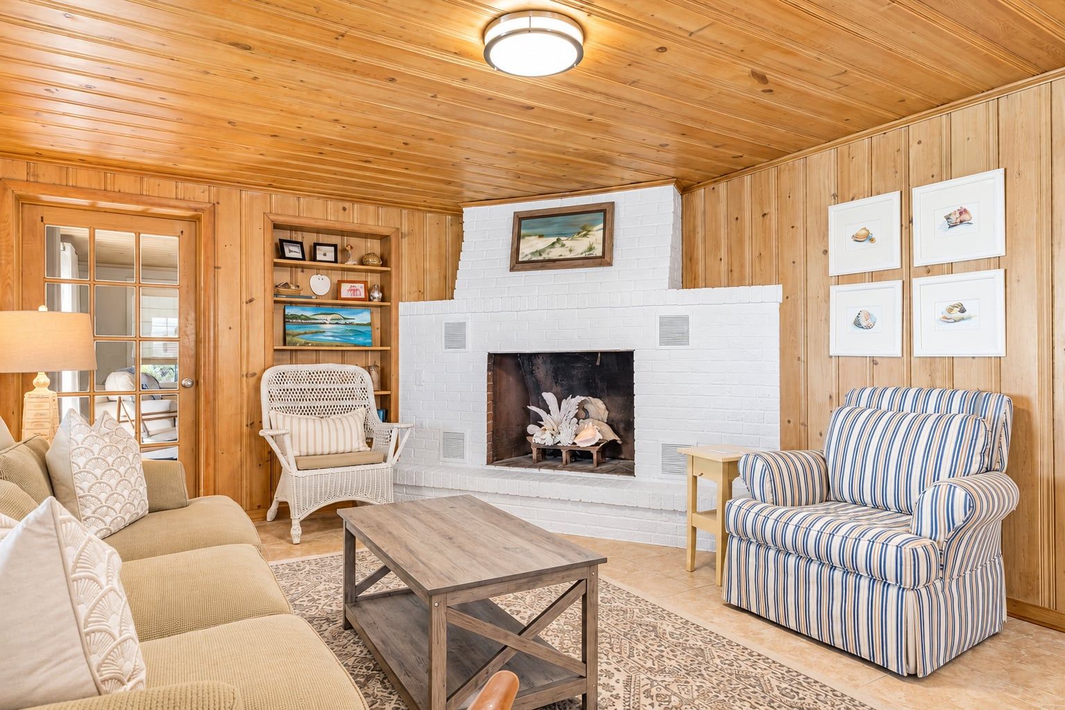 Un salon chaleureux avec une cheminée, des murs en bois, un canapé, un fauteuil à rayures et une table basse.