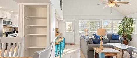 A spacious living area with a sofa, coffee table, and a dining table. There is a kitchen area with cabinets and a microwave.