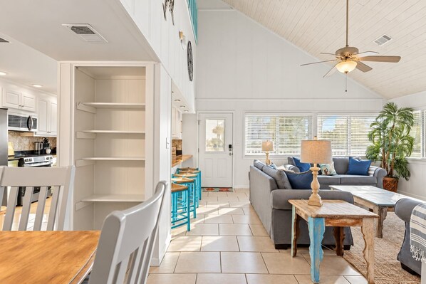 A spacious living area with a sofa, coffee table, and a dining table. There is a kitchen area with cabinets and a microwave. - Waterside Wave - 5BR/3BA Gulf Trace Home - Sleeps 14 - Private Pool & EV Charger (Santa Rosa Beach)