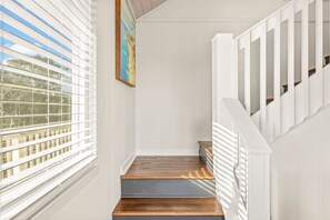 A staircase with wooden steps and white railings, leading to a landing with a painting.