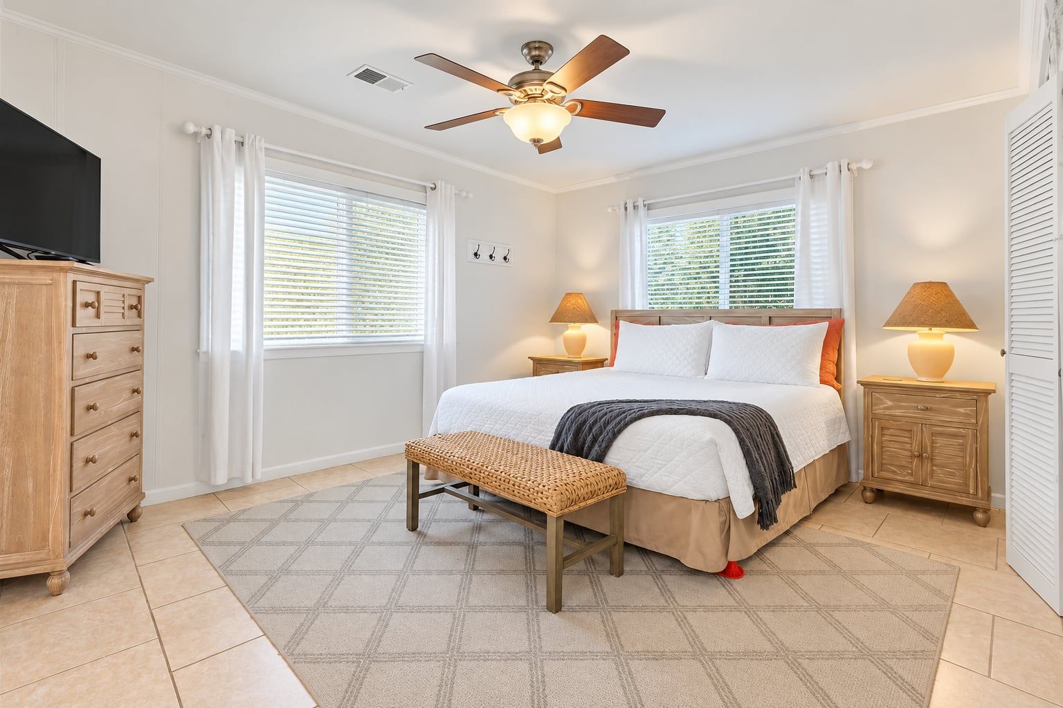 A bedroom with a bed, bedside tables, a bench, a ceiling fan, and a TV.