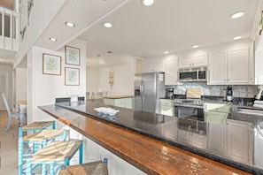 A modern kitchen with white cabinets, stainless steel appliances, and a wooden bar counter. - Waterside Wave - 5BR/3BA Gulf Trace Home - Sleeps 14 - Private Pool & EV Charger (Santa Rosa Beach)