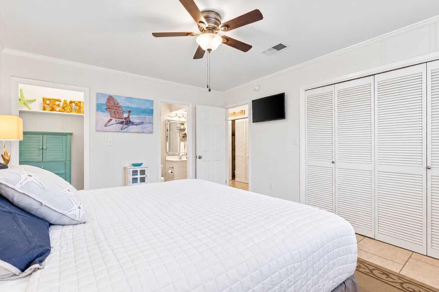 A bedroom with a bed, a ceiling fan, a TV, and a wardrobe.