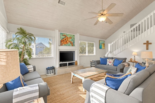 A spacious living room with a television, sofas, a coffee table, and a staircase.