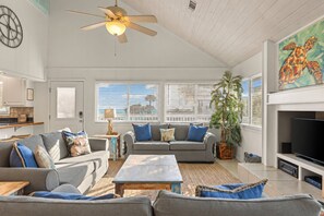 A spacious living room with a ceiling fan, a large window with blinds, a television, and a potted plant.