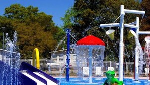 Ein Wasserpark mit einer blauen Rutsche, einer grönen Wasserspielen und einem Gebäude mit rotem Dach.