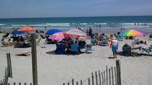 Ein Strand mit mehreren bunten Sonnenschirmen, Liegestühlen und Menschen.