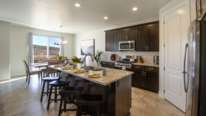 A modern kitchen with dark wood cabinets, stainless steel appliances, and a large island with bar stools. - Paseos 1146| Private Hot Tub, Pickleball Court, Access to Community Pool (Washington)