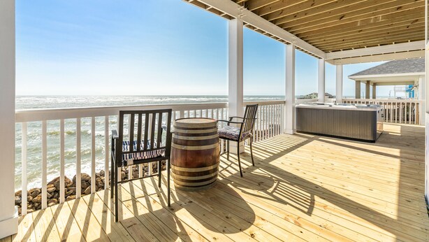 A wooden deck with a view of the ocean, a bar area, and a seating arrangement.