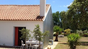 A building with a tiled roof and a small patio area with a table and chairs. - Nice country studio for 2-4p., shared pool, countryside&beach (20 km) (cercal do alentejo)