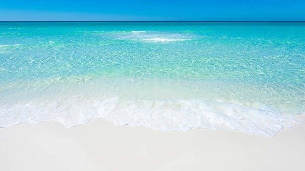 Ein Strand mit klarem, türkisblauem Wasser und weißem Sand.