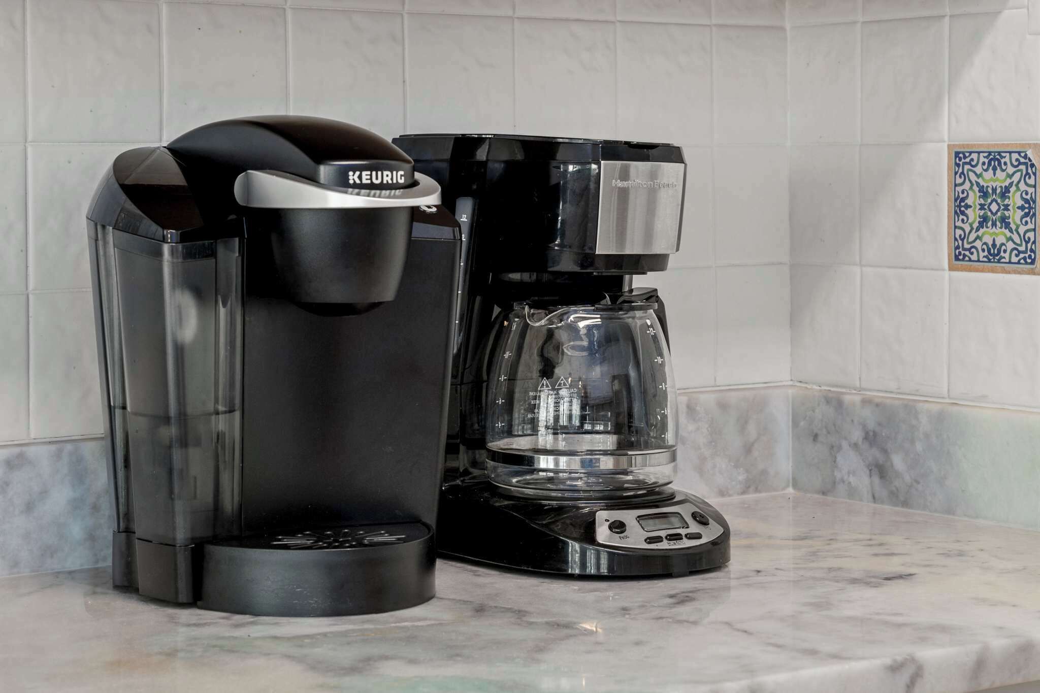 Een Keurig koffiezetapparaat met glazen kan op een marmeren aanrecht.