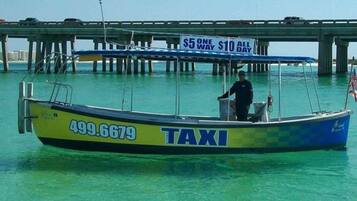 A boat with the word "TAXI" and the number 499.6679 on its side, docked near a bridge with a sign that reads "$5 ONE WAY $10 ALL DAY".