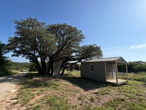 A small, single-story building with a metal roof, a wooden deck, and a staircase leading to a covered area. - Refuge Group Campground at Lake Godstone (Graford)