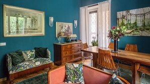 A room with teal walls, a wooden dining table, a sofa with floral cushions, and two framed artworks. - It is time to dream enjoying the steam  bath  listening lovely music  (Roma)