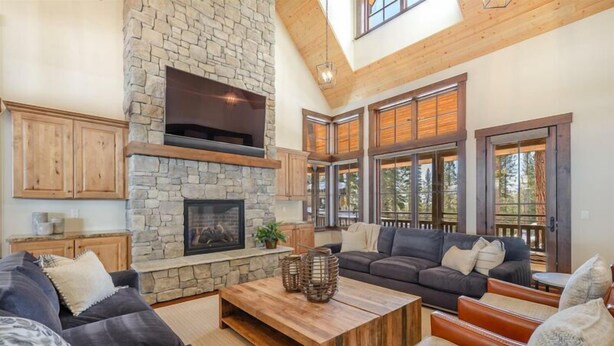 A spacious living room with a stone fireplace, wooden ceiling, and large windows offering a view of the outdoors. - NEW - Truckee Luxury Retreat - Remote Work Friendly - Sleeps 10+ (Truckee)