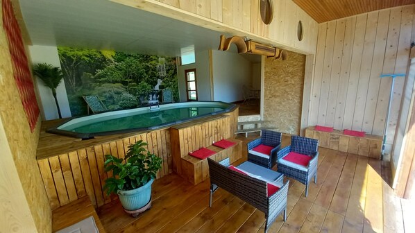Eine Holzterrasse mit Whirlpool, Korbstühlen mit roten Kissen und einem Blumentopf.