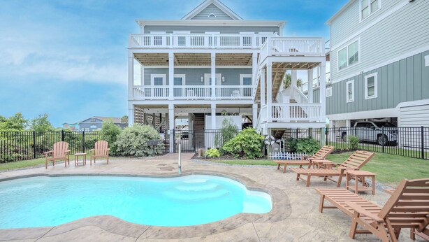 A two-story building with a pool, outdoor seating, and a fenced yard. - Pier Walker: Spacious, Beautiful Home with Amazing Ocean Views Steps from OKI Pi (Oak Island)